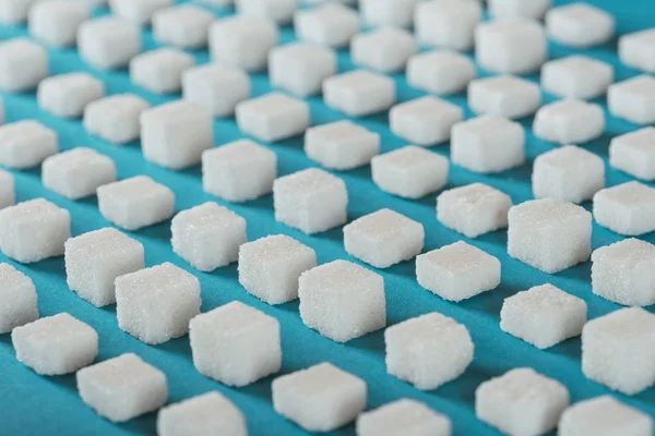 Cubetti di zucchero bianco disposti in file su superficie blu — Foto stock