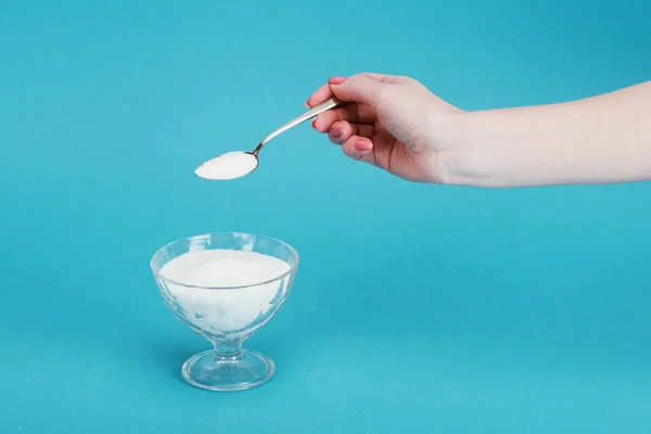 Vue recadrée de la femme ajoutant du sucre granulé dans un bol en verre sur fond bleu — Photo de stock