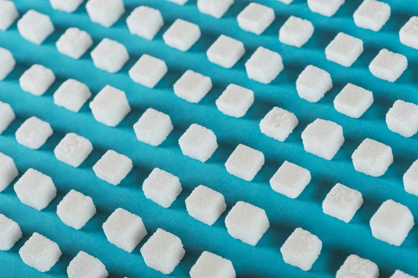 Terrones de azúcar blanco dispuestos en filas sobre la superficie azul - foto de stock