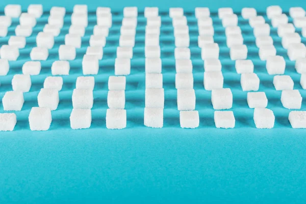 Azúcar blanco en la superficie azul dispuesta en filas horizontales - foto de stock