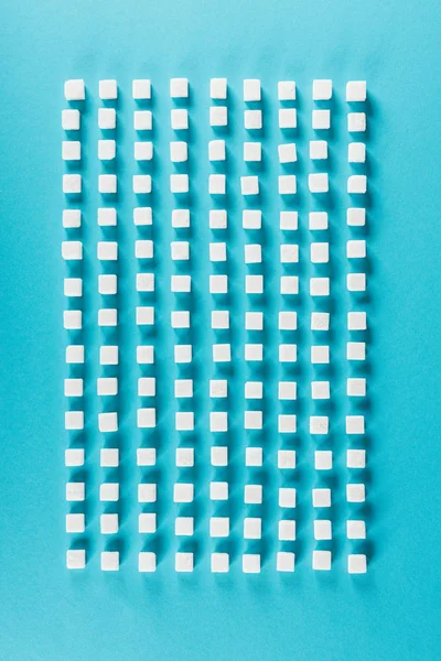 Vue de dessus des cubes de sucre blanc disposés en rangées sur la surface bleue — Photo de stock