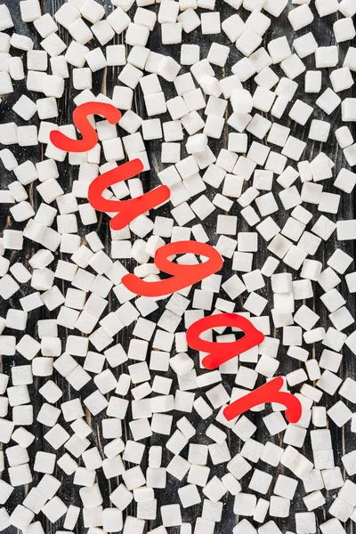 Top view of red paper cut word sugar and white sugar cubes on black surface — Stock Photo