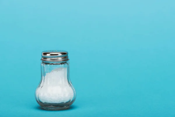 Glass salt shaker full of salt on blue background with copy space — Stock Photo