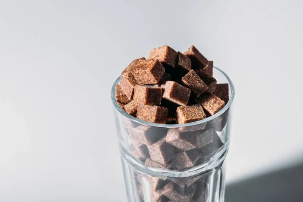Склянка, повна коричневих кубиків цукру на сірому фоні — стокове фото