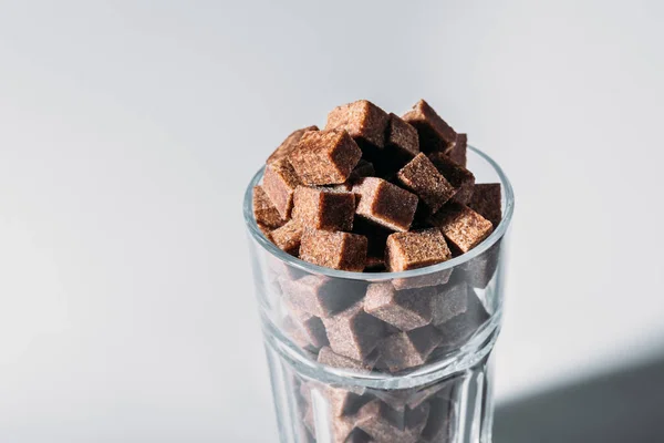 Glass full of brown sugar cubes on grey background — Stock Photo