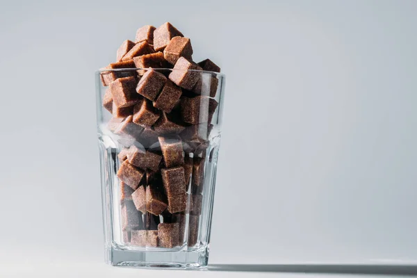 Glass with unrefined brown sugar cubes on grey background — Stock Photo