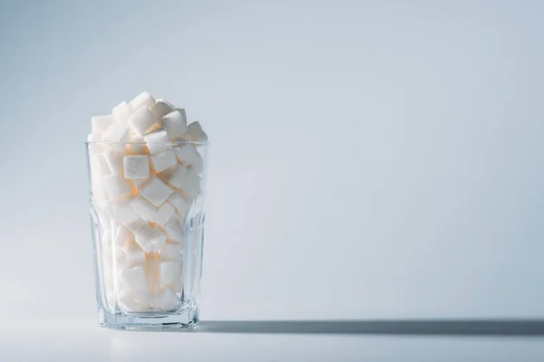 Bicchiere pieno di cubetti di zucchero bianco raffinato su sfondo grigio con spazio copia — Foto stock