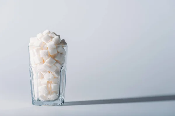 Glass full of white sugar cubes on grey background with copy space — Stock Photo