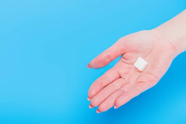 Top view of female hand with white sugar cube on blue background — Stock Photo