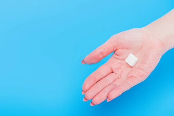 Vista superior de la mano femenina con cubo de azúcar blanco sobre fondo azul - foto de stock