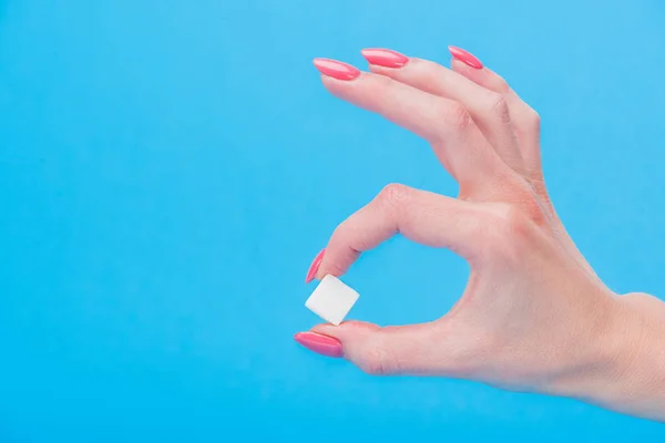 Cropped view of woman holding white sugar cube isolated on blue — Stock Photo