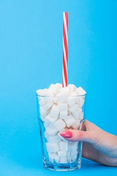 Partial view of woman holding glass with straw and white sugar cubes on blue background with copy space — Stock Photo