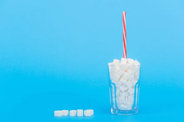 Vetro con paglia e cubetti di zucchero bianco su sfondo blu con spazio copia — Foto stock