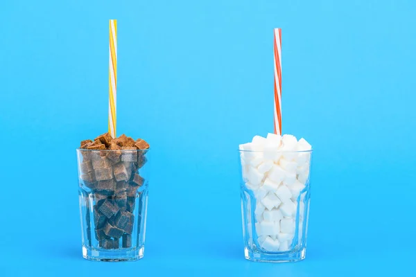 Bicchieri con cannucce e cubetti di zucchero bianco e marrone su sfondo blu — Foto stock