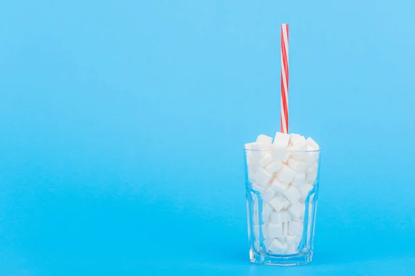 Vetro con paglia e cubetti di zucchero bianco su sfondo blu con spazio copia — Foto stock