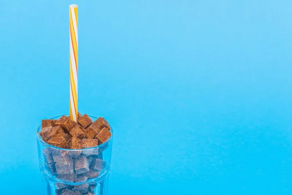 Glass with straw and brown sugar cubes isolated on blue with copy space — Stock Photo