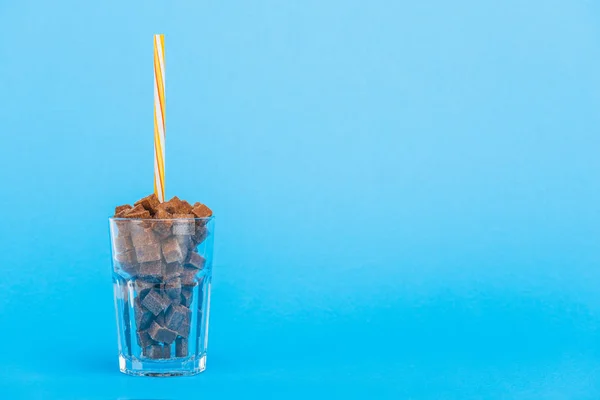 Brown sugar cubes in glass with straw on blue background with copy space — Stock Photo