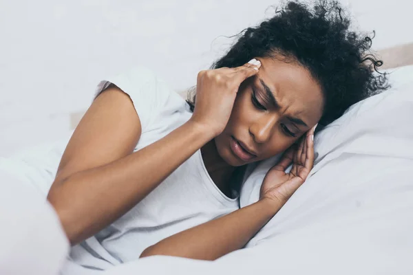 Jolie femme afro-américaine souffrant de maux de tête alors qu'elle était couchée au lit — Photo de stock