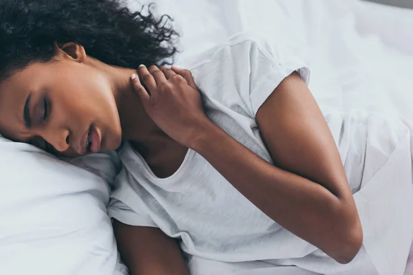 Atractiva mujer afroamericana que sufre de dolor de cuello mientras está acostada en la cama con los ojos cerrados — Stock Photo