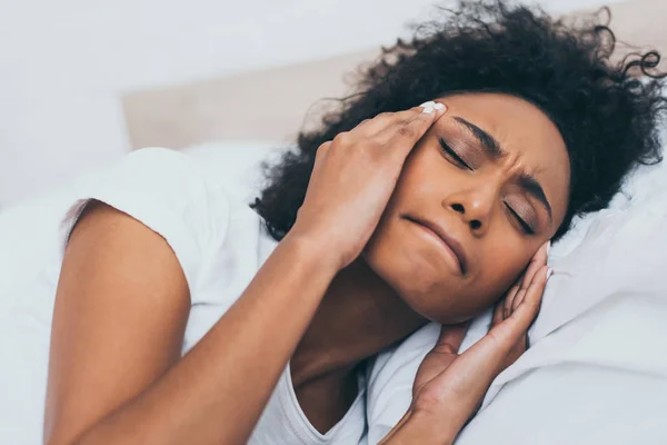 Jeune femme afro-américaine couchée au lit et souffrant de maux de tête — Photo de stock