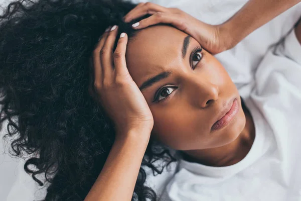 Hermosa mujer afroamericana mirando hacia arriba mientras que sufre de dolor de cabeza - foto de stock
