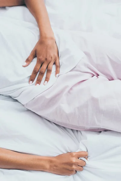 Vista recortada de la mujer afroamericana que sufre de dolor abdominal mientras está acostada en la cama - foto de stock