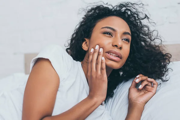 Unhappy african american woman suffering from toothache while lying in bed — Stock Photo