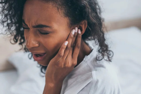 Giovane donna afroamericana che soffre di dolore all'orecchio in camera da letto con gli occhi chiusi — Foto stock