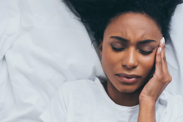 Вид зверху симпатична афроамериканець жінка страждає від головного болю, лежачи в ліжку — стокове фото