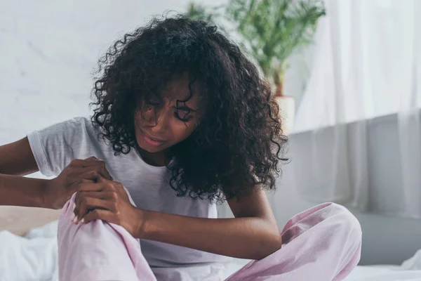Unhappy african american woman suffering from foot pain in bedroom — Stock Photo