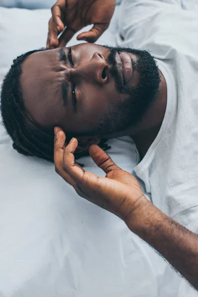 Unhappy african man suffering from headache while lying in bed — Stock Photo