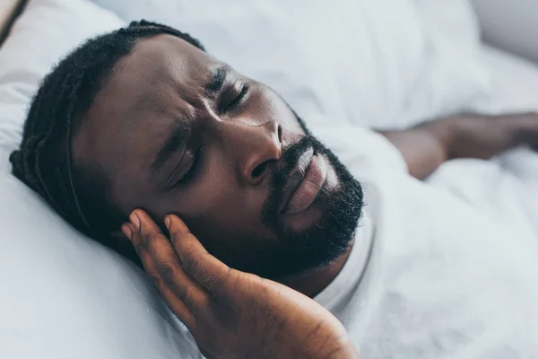 Exausto afro-americano sofrendo de dor de cabeça enquanto estava deitado na cama — Fotografia de Stock