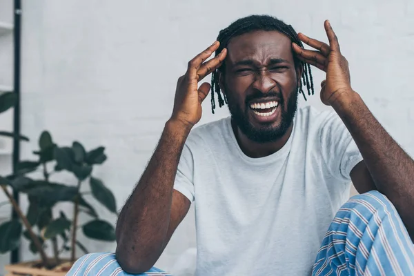 Gritando hombre afroamericano que sufre de dolor de cabeza en el dormitorio - foto de stock