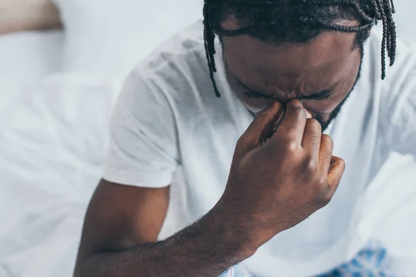 Unhappy african american man holding hand near face while suffering from headache in bedroom — Stock Photo