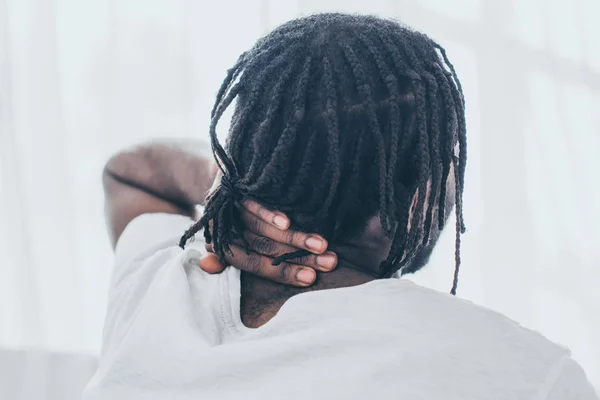 African american man with dreadlocks holding hand on neck while suffering from neck pain — Stock Photo