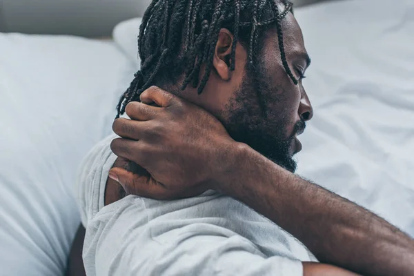Giovane uomo afroamericano con dreadlocks che soffre di dolore al collo in camera da letto — Foto stock