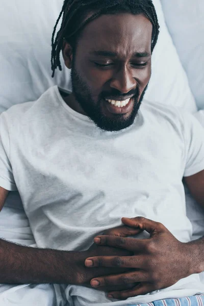 Esausto uomo afro-americano che soffre di mal di stomaco in camera da letto — Foto stock