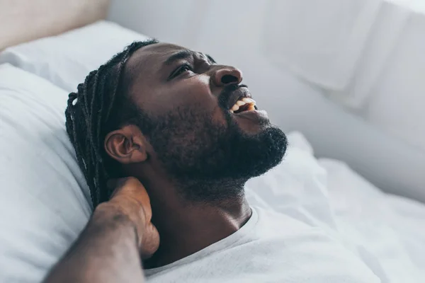 Screaming african american man suffering from neck pain in bedroom — Stock Photo