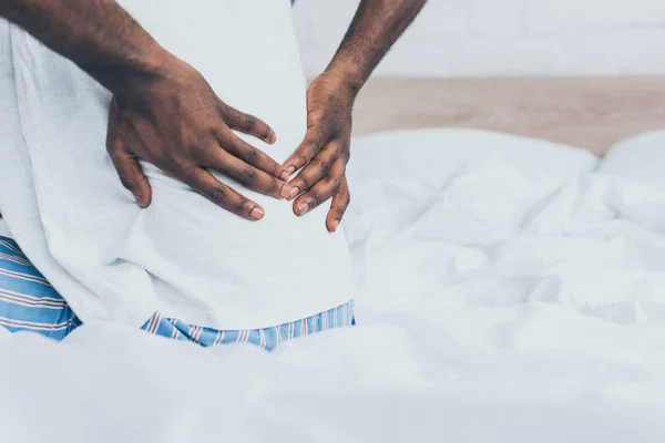 Abgeschnittene Ansicht eines an Rückenschmerzen leidenden afrikanisch-amerikanischen Mannes im Schlafzimmer — Stockfoto