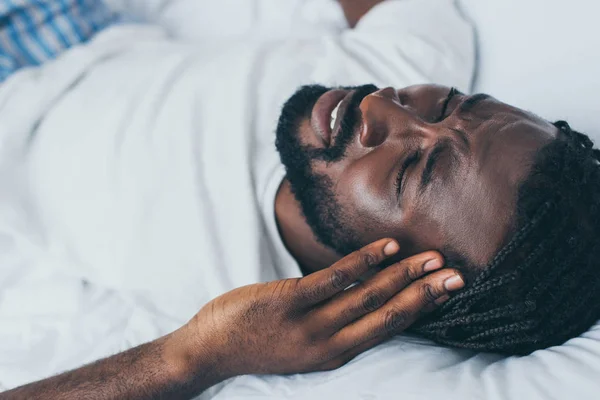 Vista aérea del hombre afroamericano que sufre de dolor de cabeza en el dormitorio - foto de stock