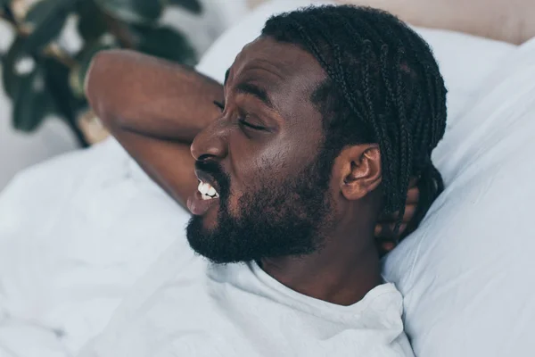 Malheureux homme afro-américain souffrant de douleur au cou tout en étant couché dans le lit — Photo de stock