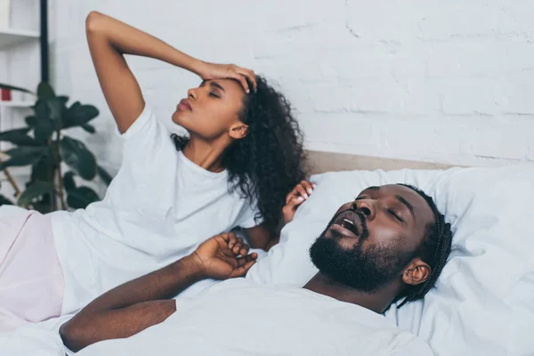 Jeune femme afro-américaine souffrant de maux de tête tout en étant couché près de ronflement mari — Photo de stock