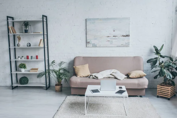 Spazioso soggiorno con divano, rack, piante e tavolo con dispositivi digitali — Foto stock