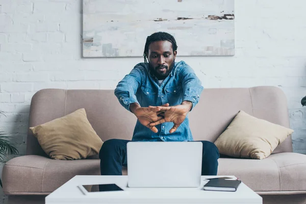 Красивий афроамериканський чоловік сидить на дивані біля столу з цифровими пристроями — стокове фото