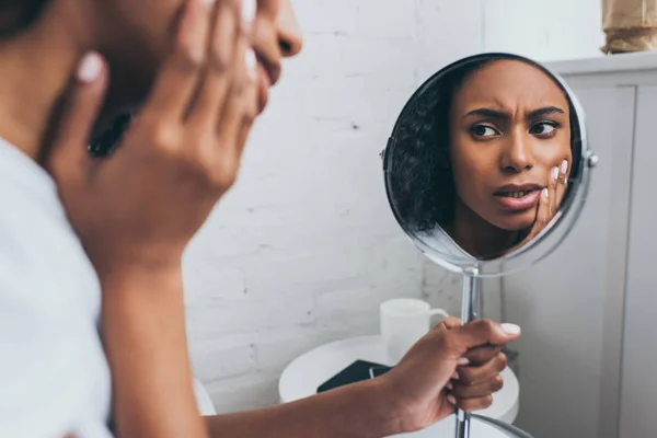 Jolie femme afro-américaine regardant miroir tout en souffrant de douleur dentaire — Photo de stock