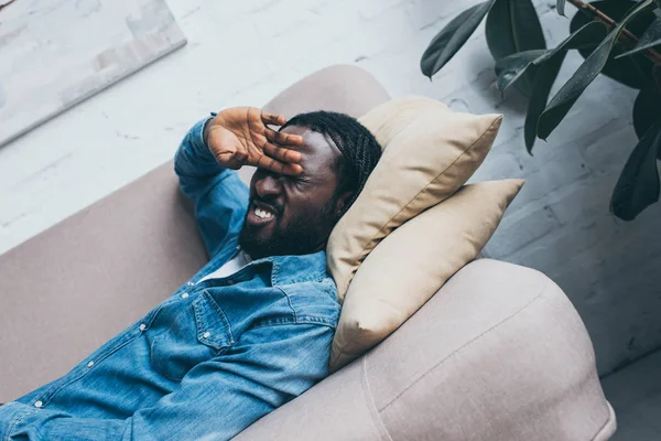 Esausto uomo afroamericano sdraiato sul divano e affetto da mal di testa — Foto stock
