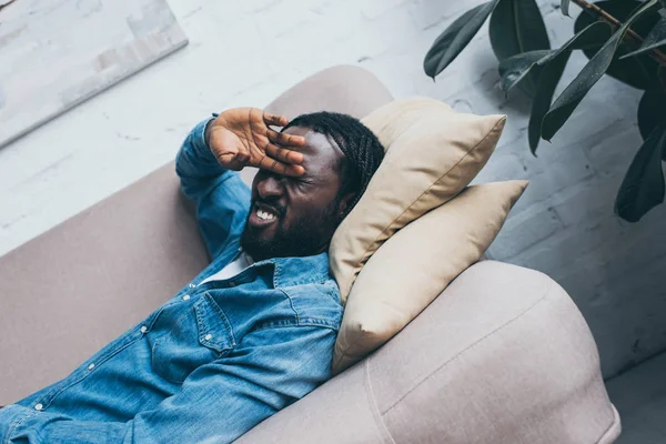 Exhausted african american man lying on sofa and suffering from headache — Stock Photo