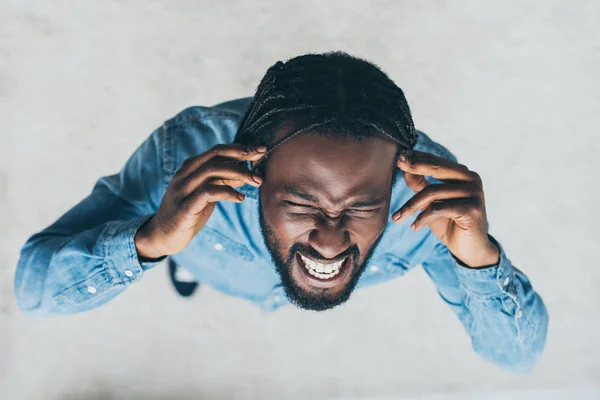 Overhead view of african man holding hands near head while suffering from headache — Stock Photo