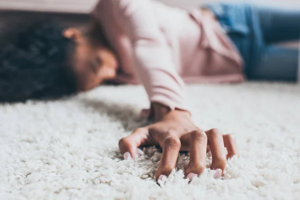 Selective focus of african american woman suffering from pain while lying on floor — Stock Photo