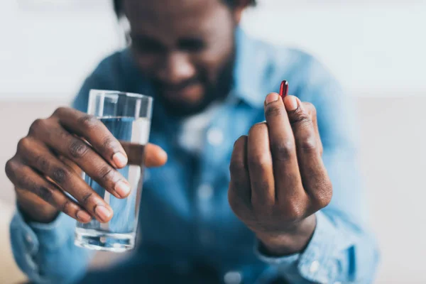 Enfoque selectivo del hombre afroamericano que sufre de dolor y celebración de vaso de agua y píldora - foto de stock